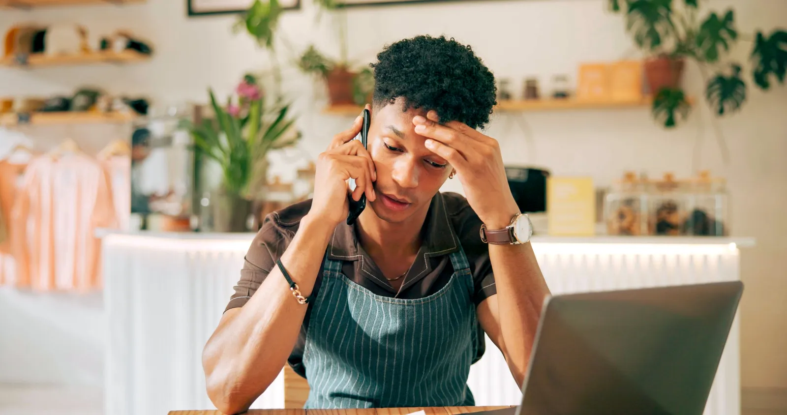 A business owner on a phone call beside a laptop.