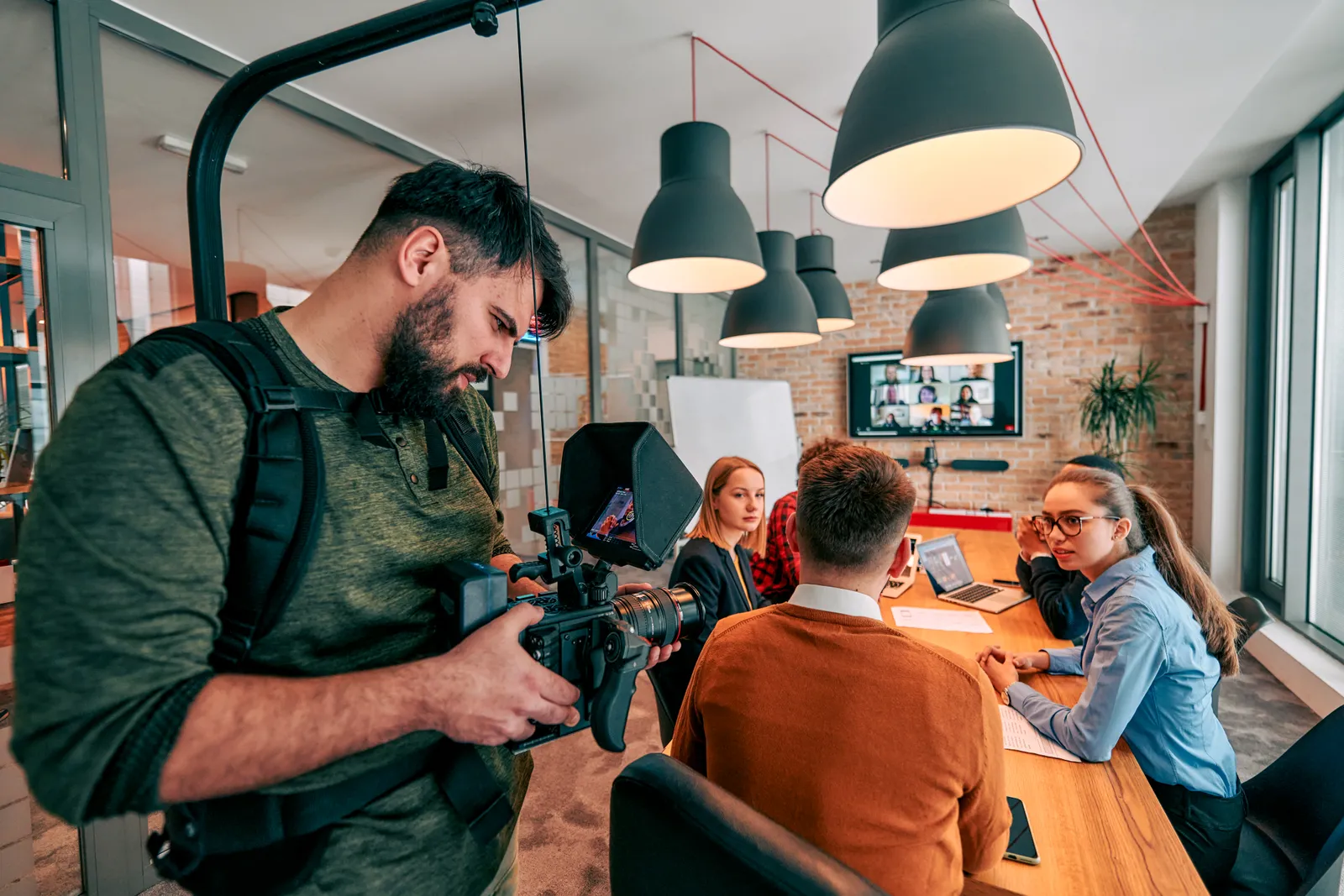A videographer filming a business meeting in a modern office.