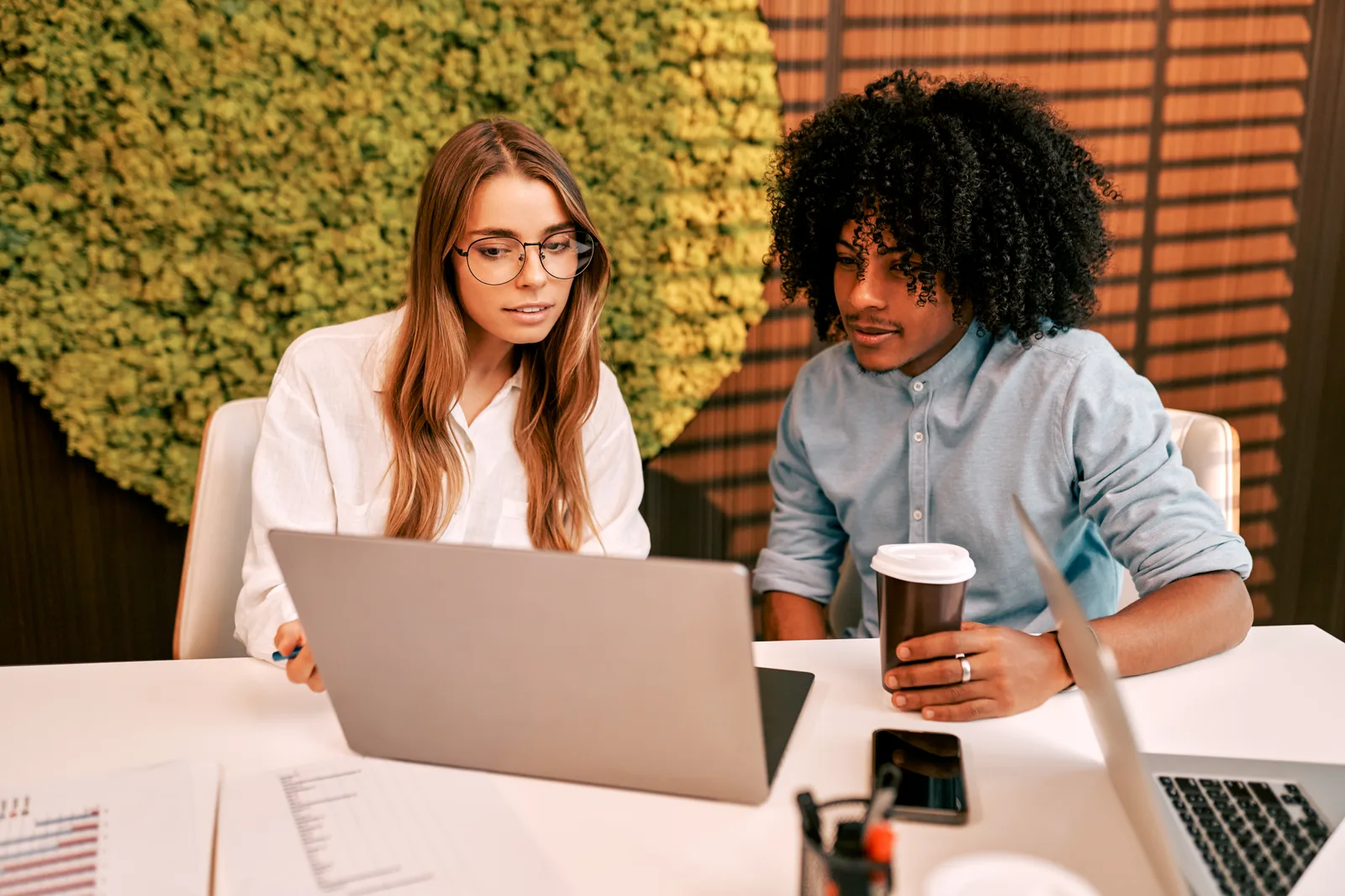 Two people reviewing marketing work together at a laptop.