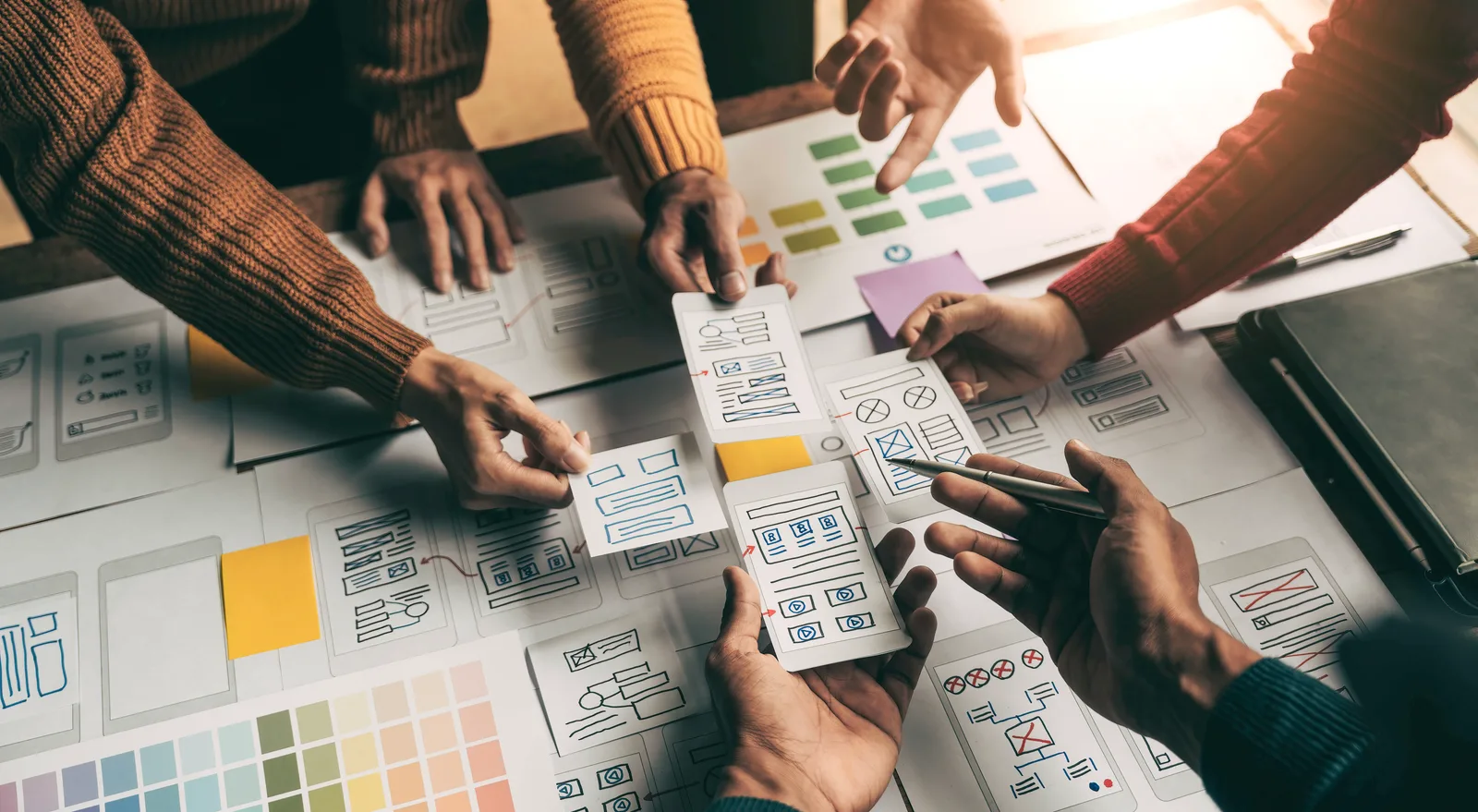 Hands arranging website wireframes during a planning session.